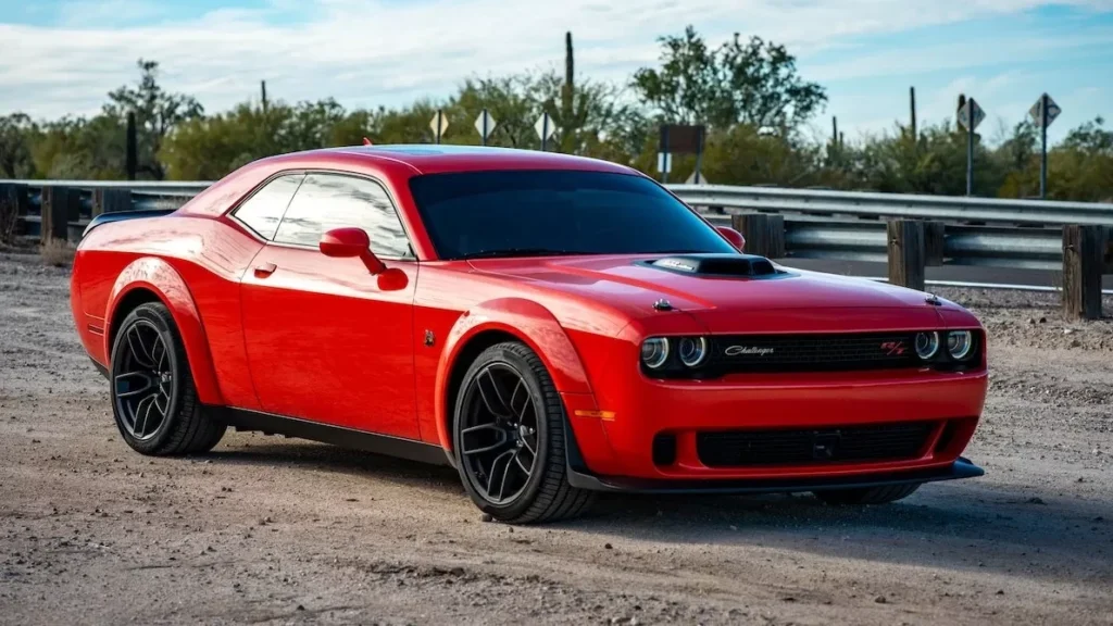 Vibrant red Dodge Challenger parked on a rural road under a clear sky