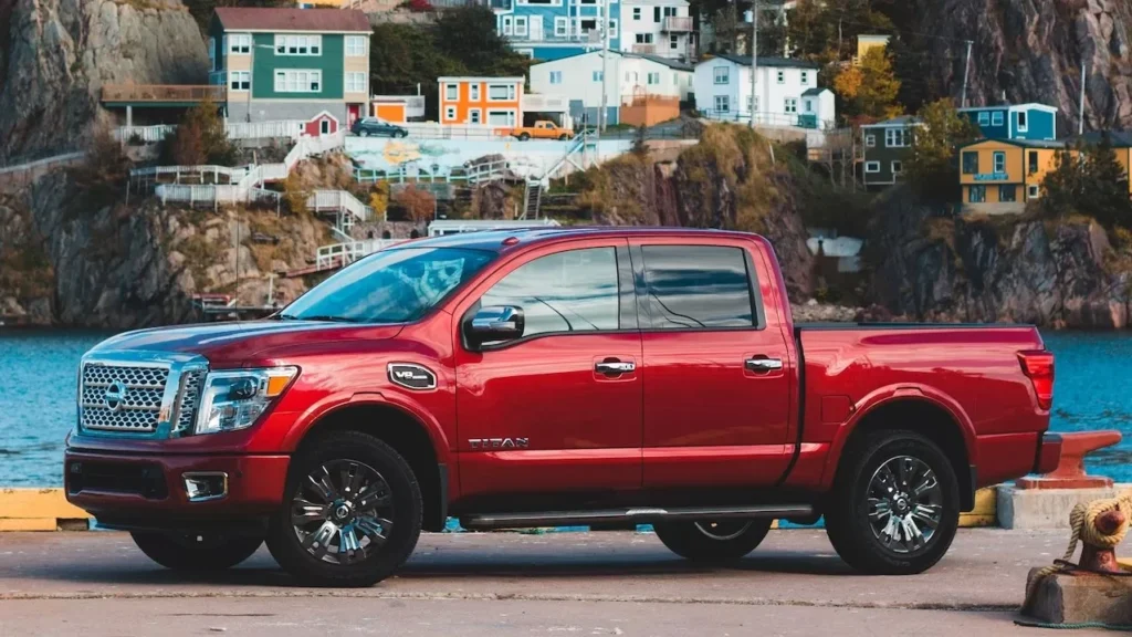 A red pickup truck parked near colorful hillside houses by the sea