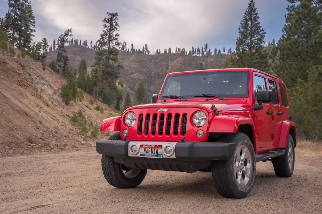 Red Jeep parked on dirt road with mountainous forest backdrop, ideal for travel and adventure themes