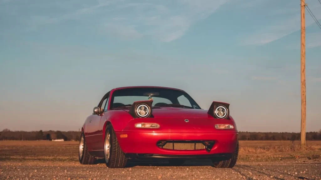 Red sports car with pop-up headlights captured on a country road during sunset