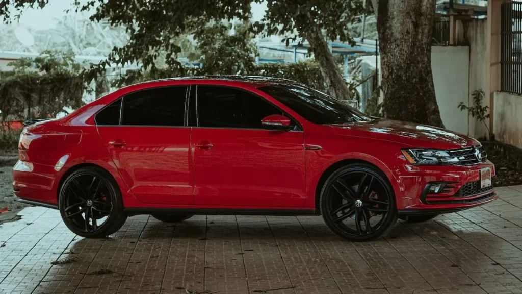 A striking red sedan parked under a tree on a paved surface, exuding style and elegance.