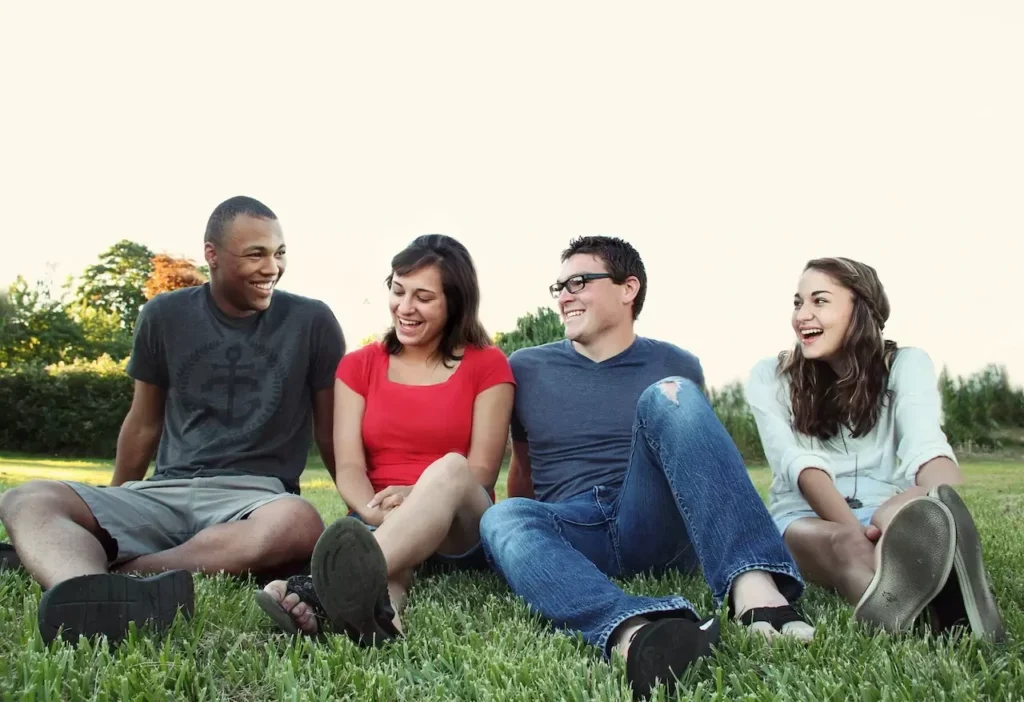 A group of young adults smiling while sitting on grass in a sunny park, enjoying friendship and leisure