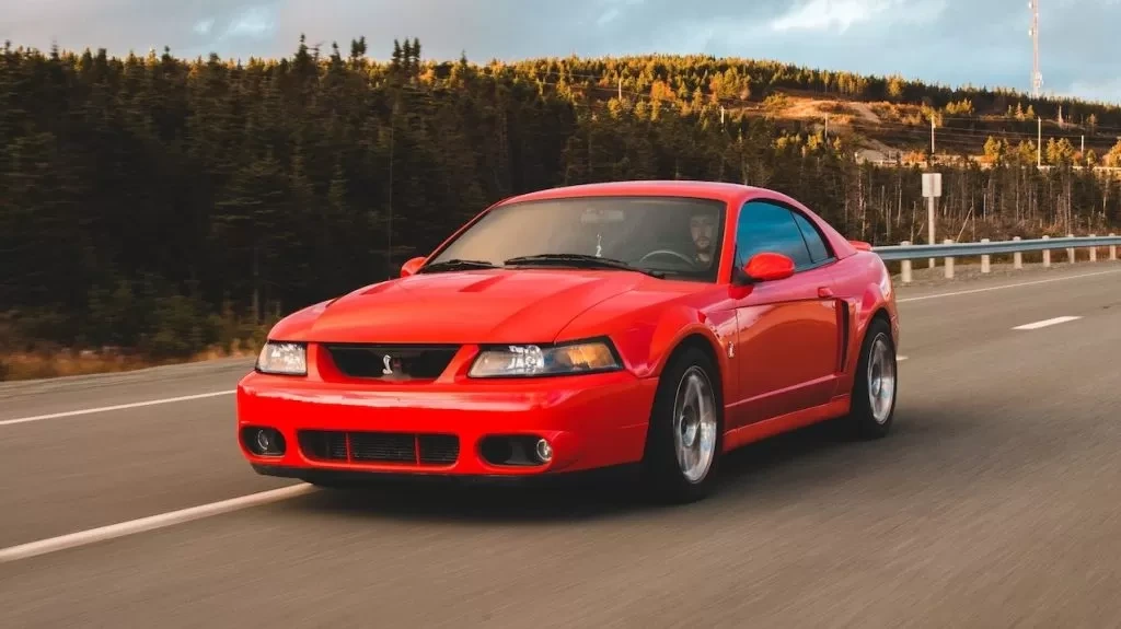 Red sports car speeding on a scenic highway amidst forest landscape at sunset