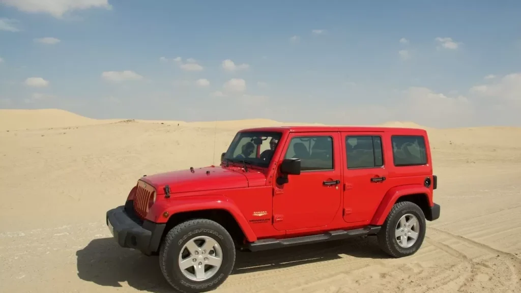 Side view of a red SUV parked in a vast desert under a clear blue sky. Ideal for travel and adventure themes