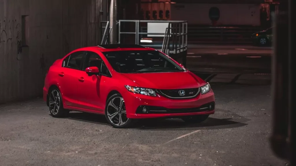 A stylish red sedan parked in an industrial urban area at night, illuminated by city lights
