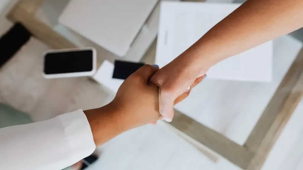 Two people shaking hands over a desk with modern tech, symbolizing a successful business agreement