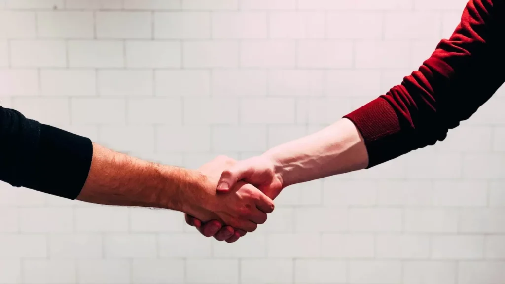 Two person shaking hands near white painted wall