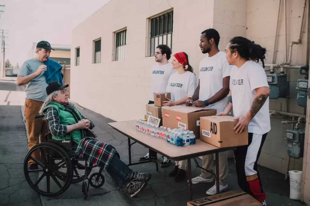 Volunteers assist a senior adult in a wheelchair by distributing aid packages outdoors