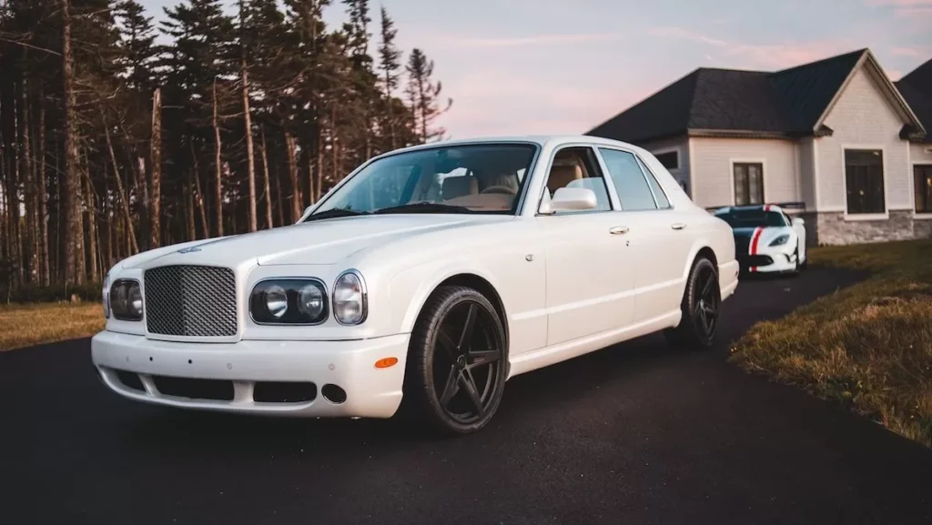 A classic luxury white car parked on a suburban driveway beside a modern house