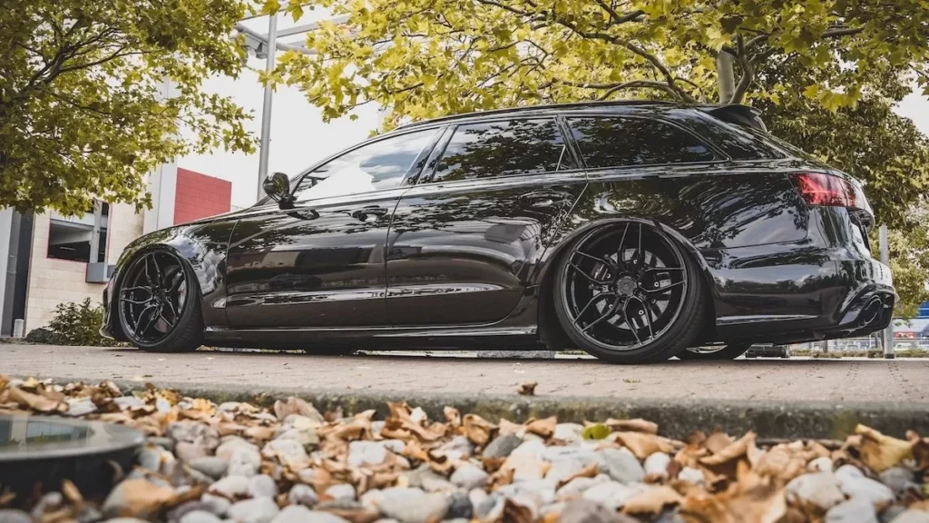 Black sedan on road with autumn leaves, showcasing modern automotive design
