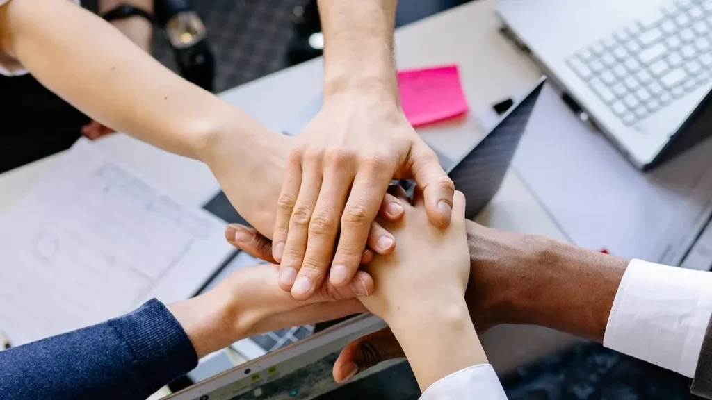 A diverse group of professionals stacking hands over a table symbolizing teamwork and collaboration