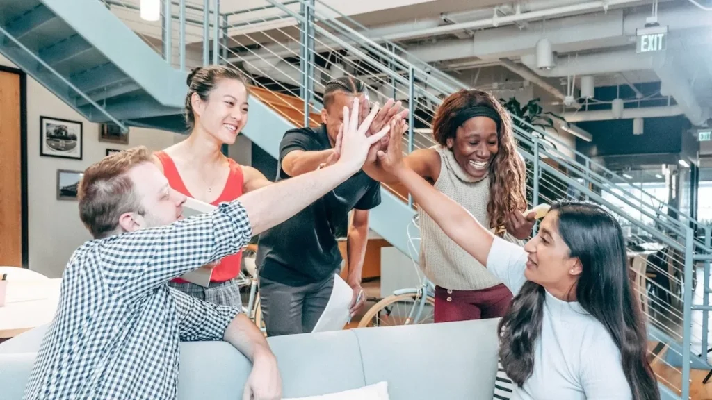 A diverse team celebrates success with a high-five in a modern office setting