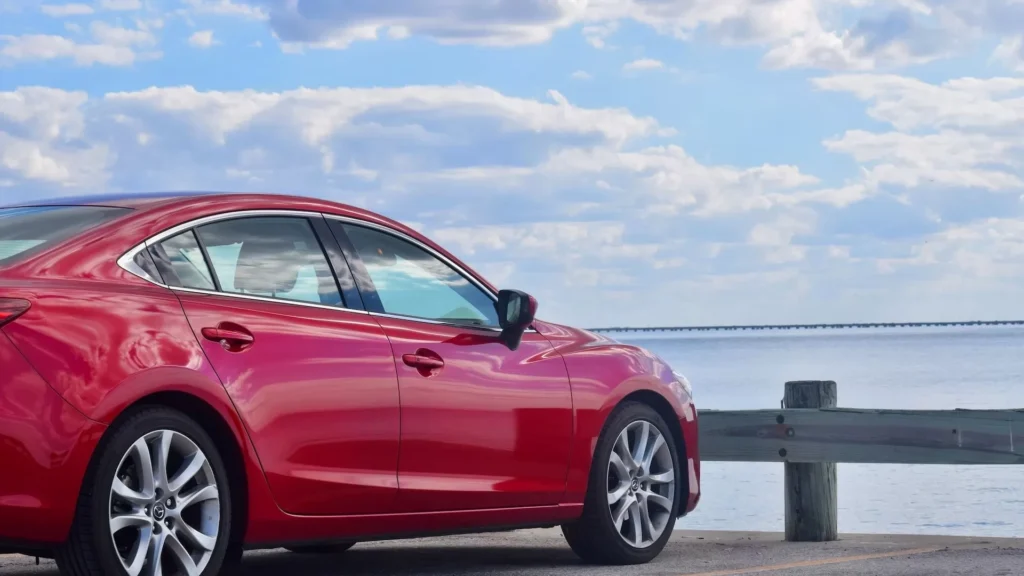 A red car parked on a road by the water