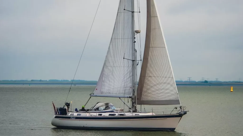 A solitary sailboat gracefully cruises on a calm sea under cloudy skies