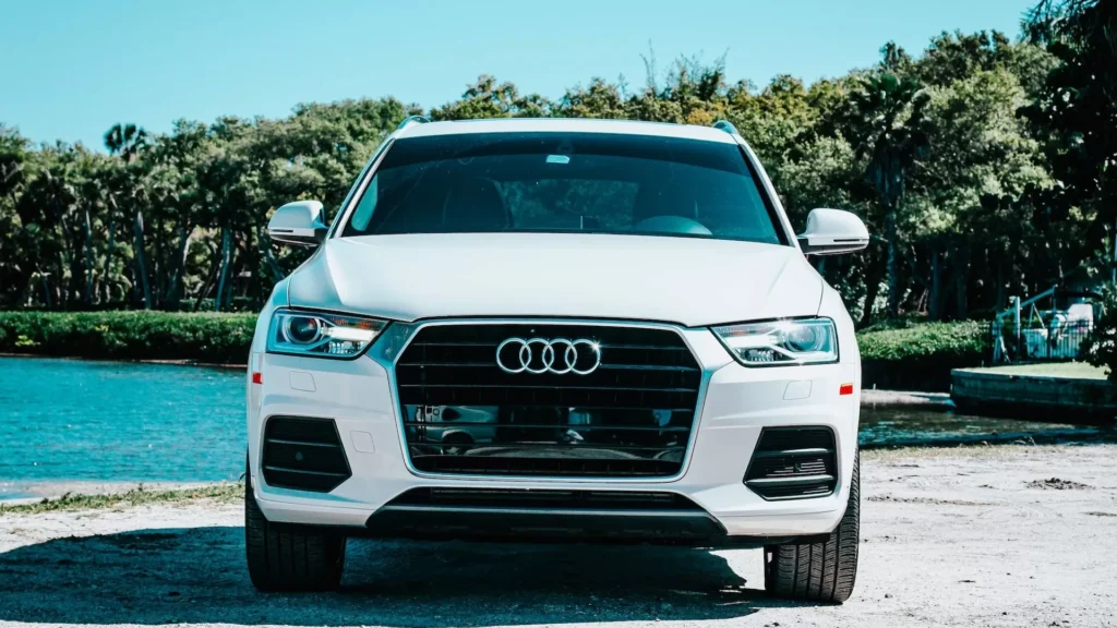 A white Audi parked in front of a body of water