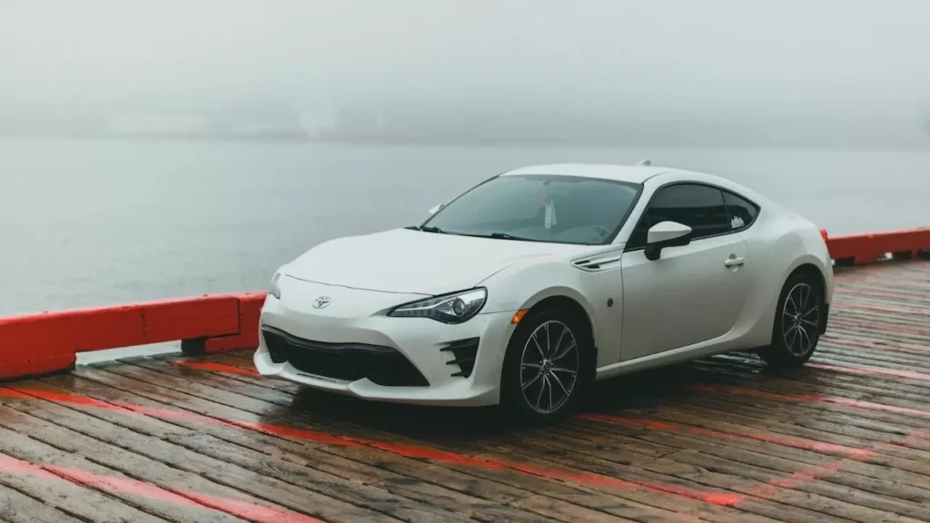A sleek white coupe parked on a wooden dock by the water under foggy conditions