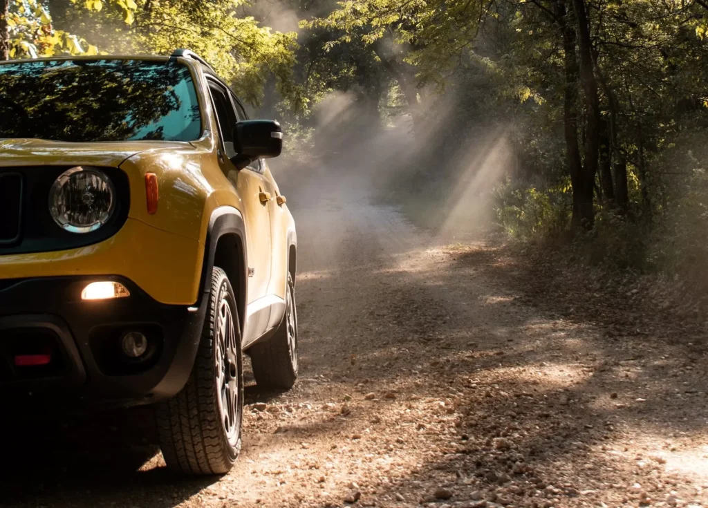 A yellow Jeep on a dirt road with trees on either side of it