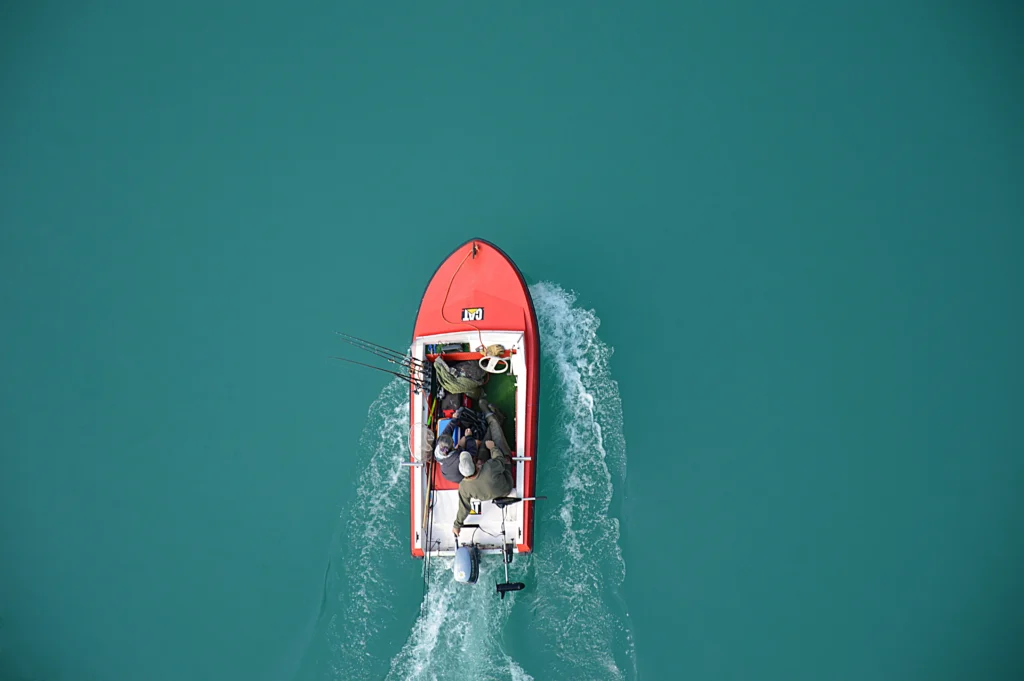 Top view of a red motorboat with fishermen navigating open turquoise waters