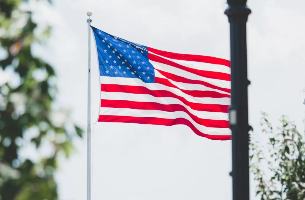 An American flag flying in the wind next to a lamp post