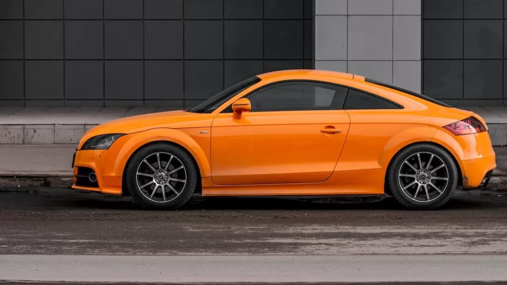 An orange coupe car parked on a city street against a modern building facade