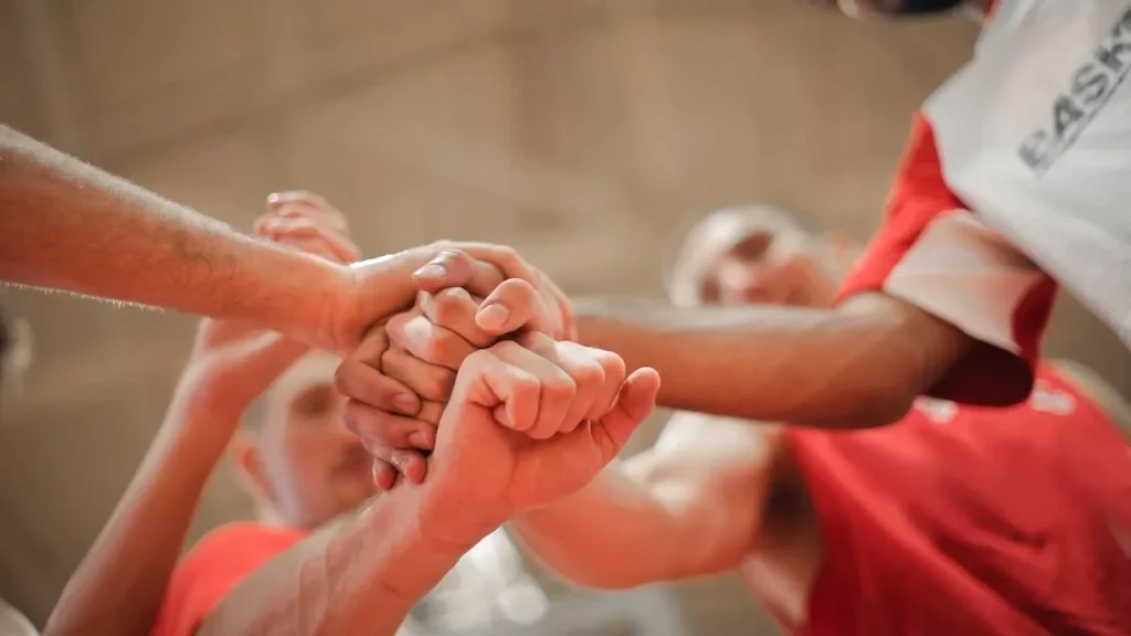 A group of athletes stacking hands, symbolizing unity and teamwork on the basketball court