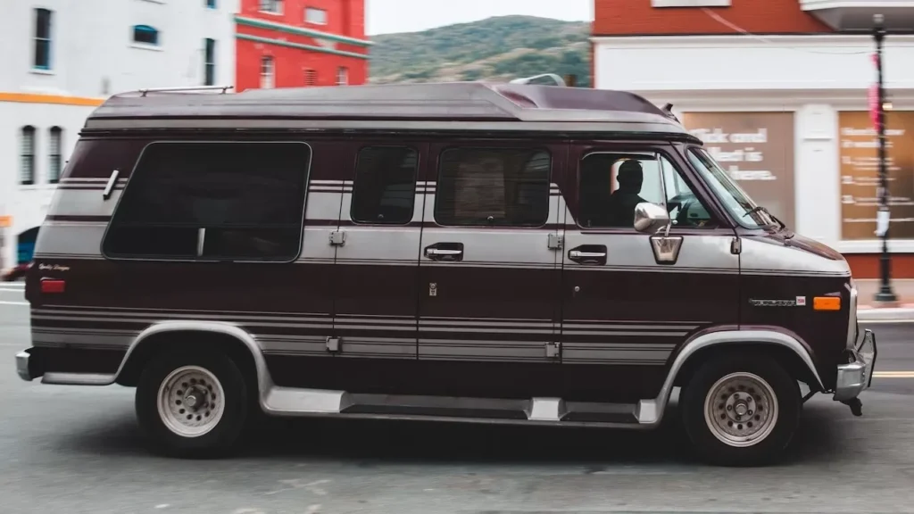 A classic minivan travels along a vibrant urban street