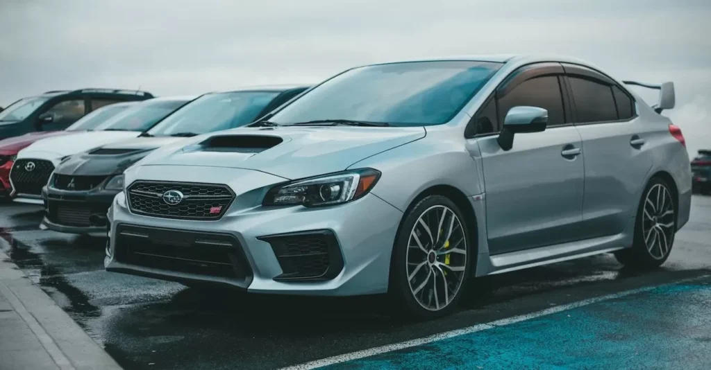 A silver Subaru WRX parked in a city parking lot with other cars on a rainy day