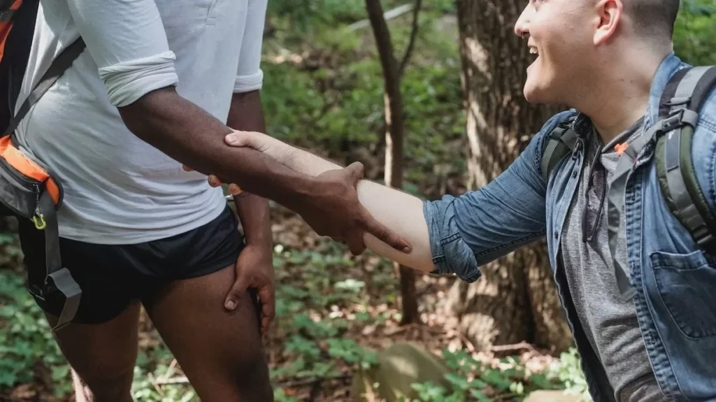 Two hikers helping each other up a trail in a vibrant forest setting