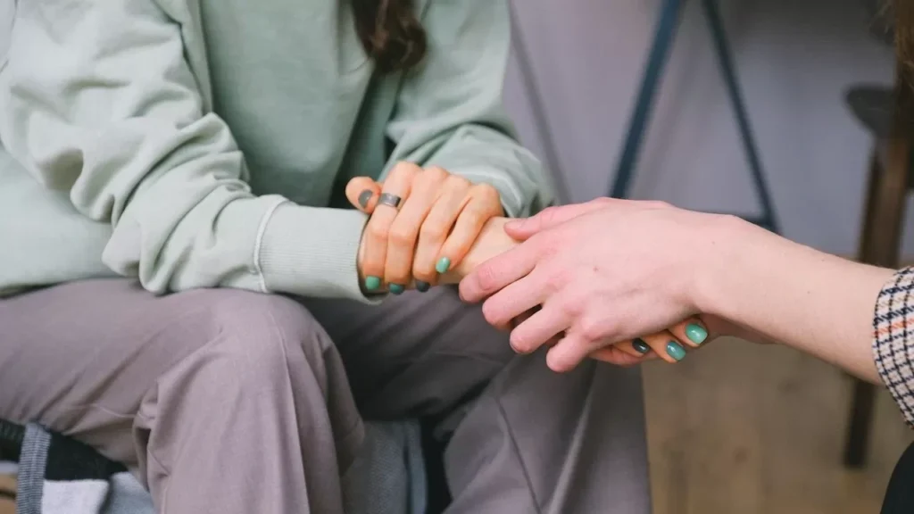 Close-up of two people holding hands during a comforting therapy session