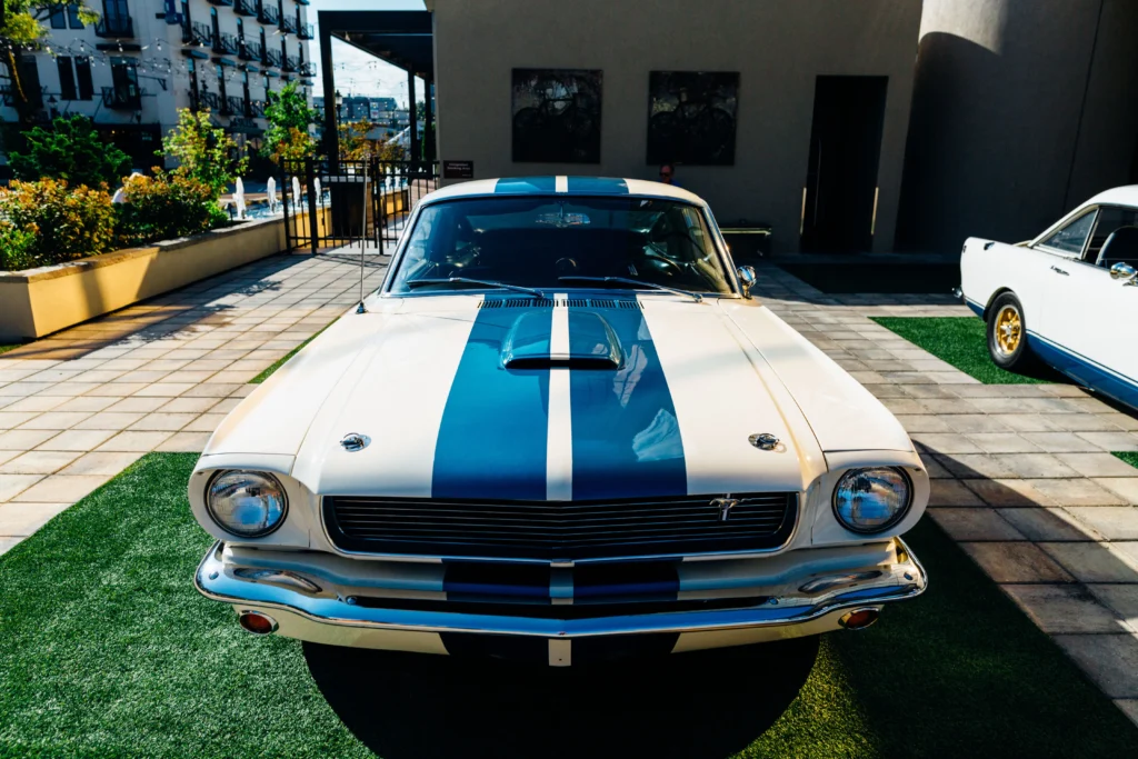 A vintage Ford Mustang with blue racing stripes, parked outdoors in sunlight