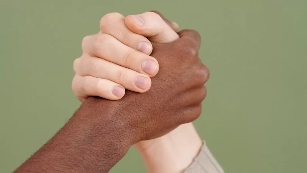 Close-up of diverse hands clasped together against a green background symbolizing unity