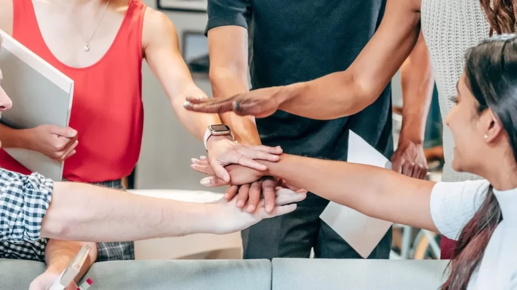 A diverse group of coworkers uniting hands in an office setting, symbolizing teamwork and collaboration