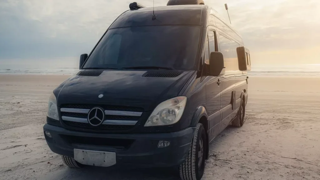 A black camper van parked on a serene beach during sunset, ideal for travel enthusiasts