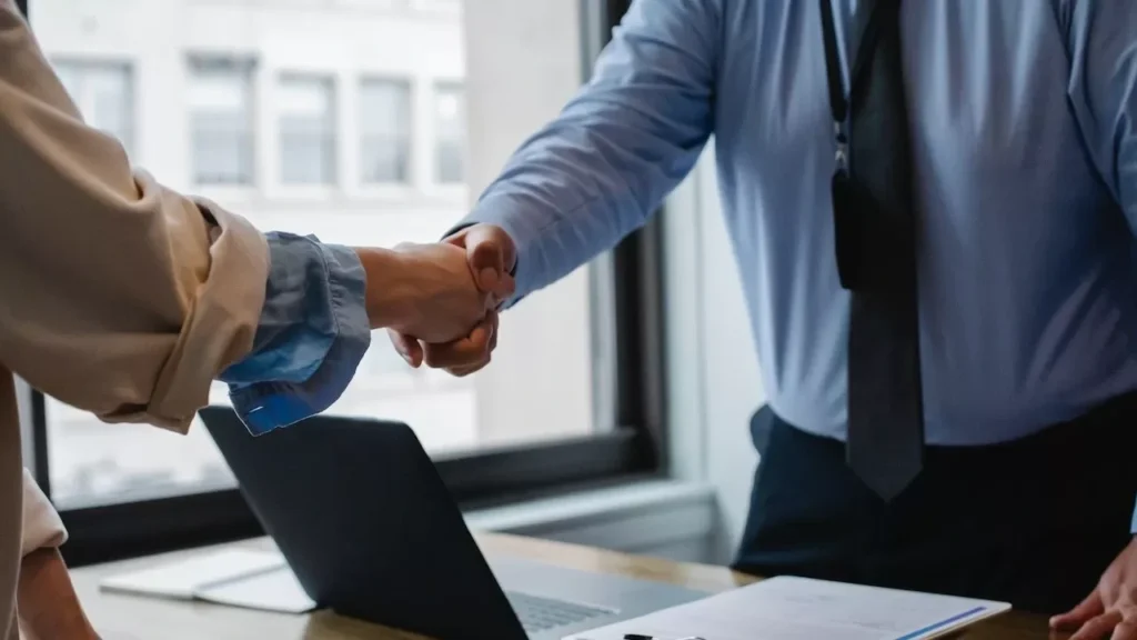 Two business professionals shaking hands in a modern office setting, symbolizing successful collaboration