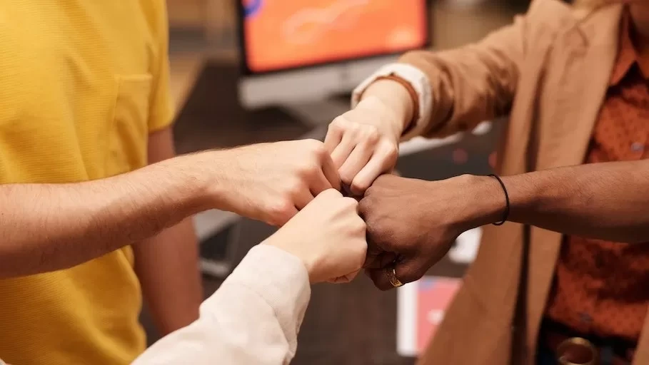 Group of colleagues fist bumping to celebrate teamwork and unity in a modern office setting