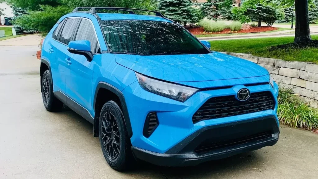 Bright blue SUV parked on a driveway surrounded by lush greenery on a cloudy day.