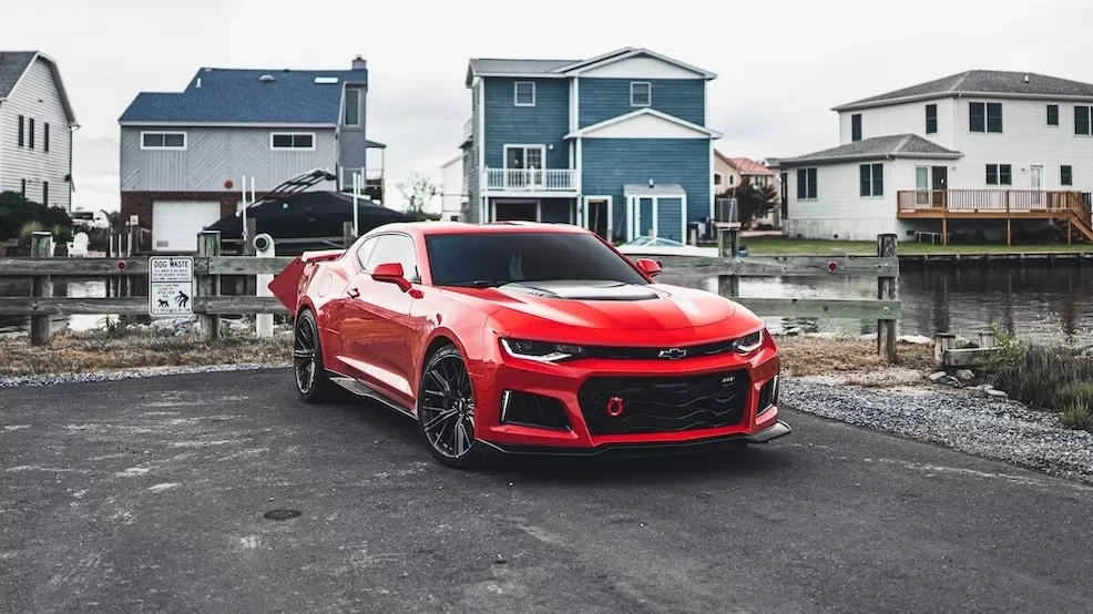 Sleek red sports car parked in front of waterfront homes on a cloudy day