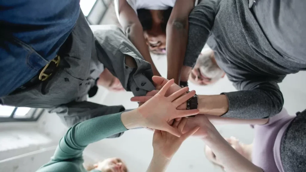 Low angle view of a diverse group uniting hands indoors, symbolizing teamwork and collaboration