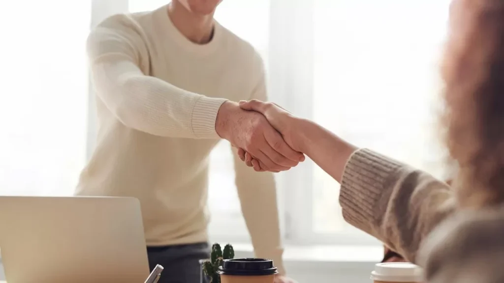 Close-up of professionals shaking hands over coffee in a modern office