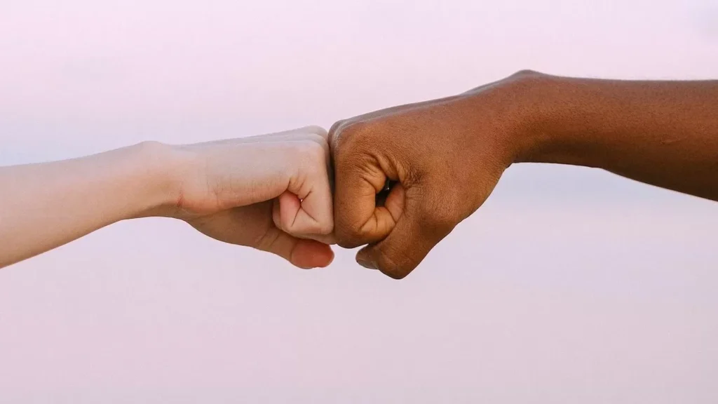 Two diverse hands fist bump against a soft pastel background