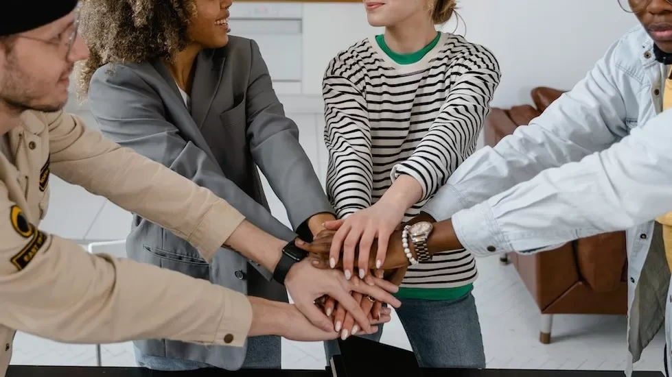 A group of diverse coworkers uniting hands to symbolize teamwork in a modern office