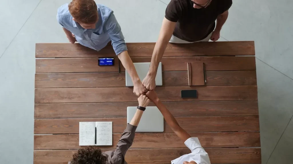 A diverse group of professionals engaging in a teamwork celebration with a fist bump over a wooden table indoors
