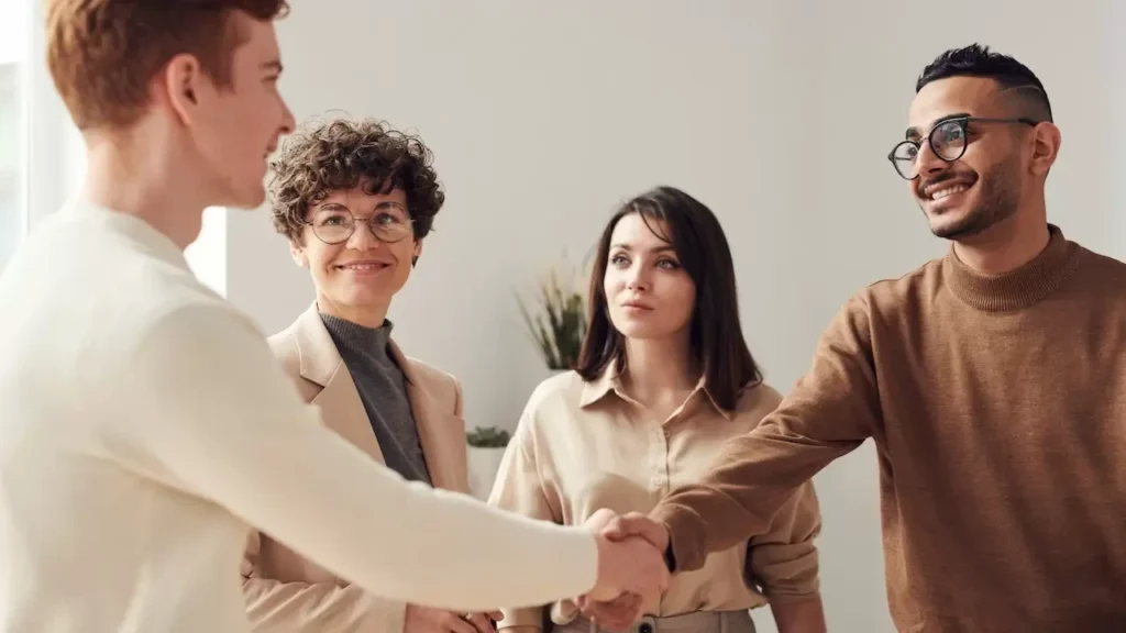 Four colleagues in an office handshake demonstrating teamwork and cooperation
