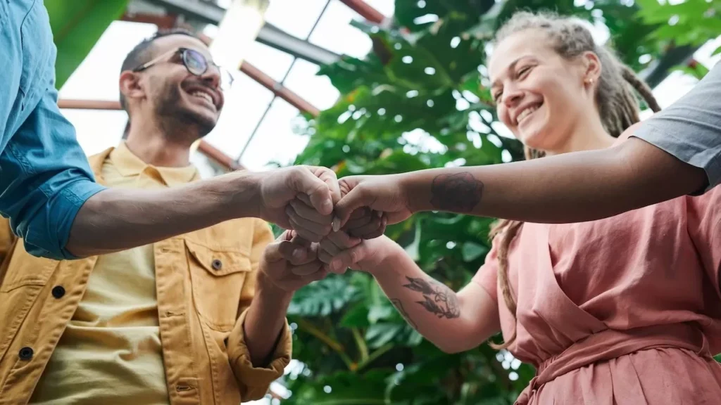 A group of young adults celebrating teamwork with a fist bump in a lush outdoor setting