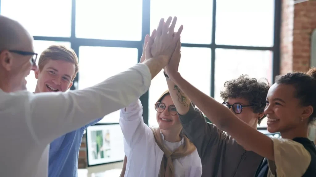 A diverse team of professionals celebrating success with a high five in a modern office