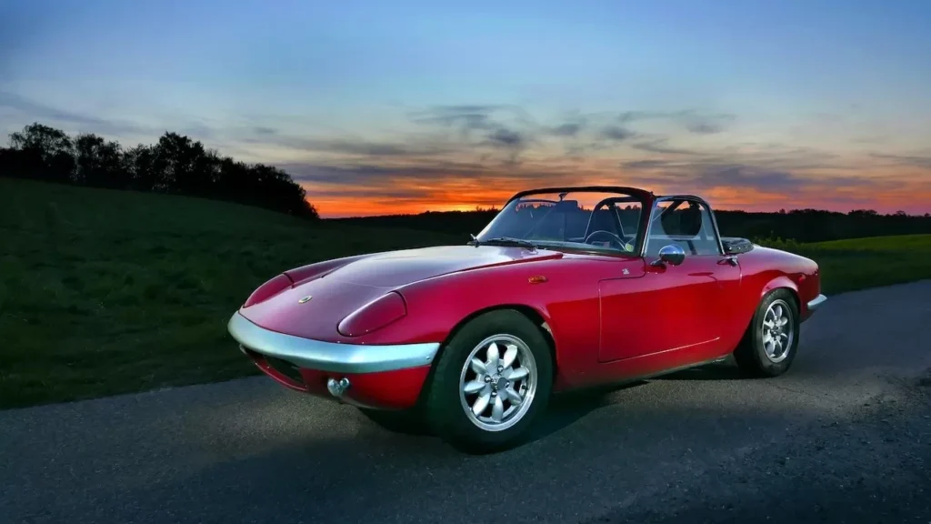 A classic red convertible sports car parked on a road against a stunning sunset backdrop