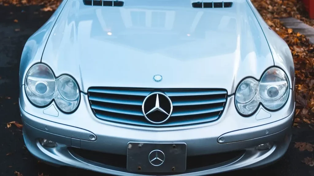 A classic Mercedes-Benz sedan parked in front of a house surrounded by fall leaves