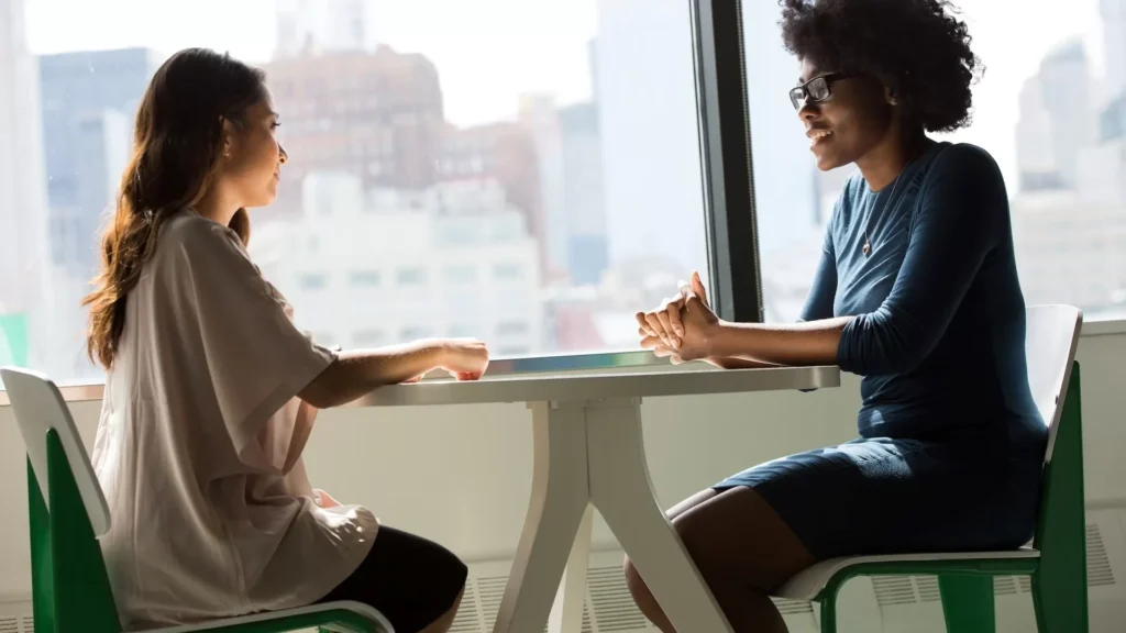 Two women sitting beside table and talking