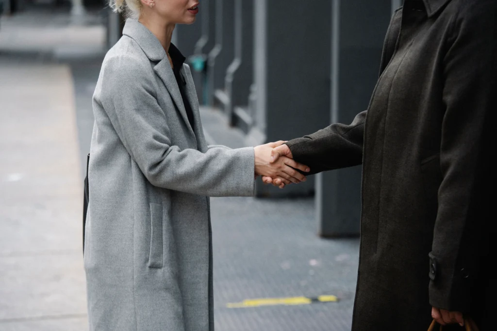Two business people in coats shaking hands on an urban street