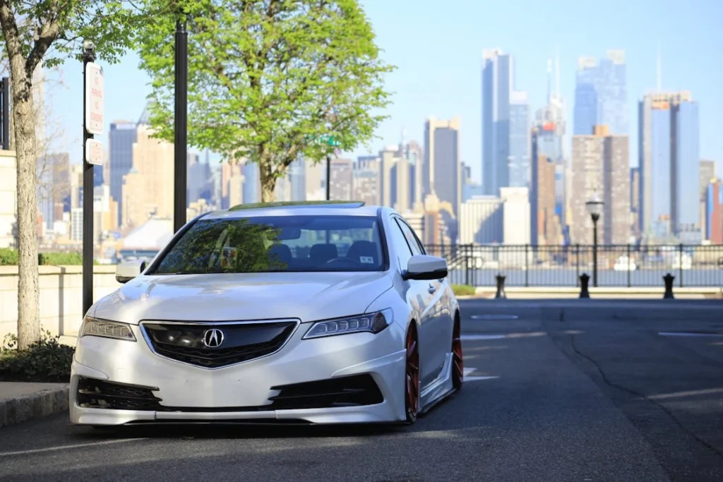 A customized silver Acura parked with a city skyline backdrop, showcasing urban car culture